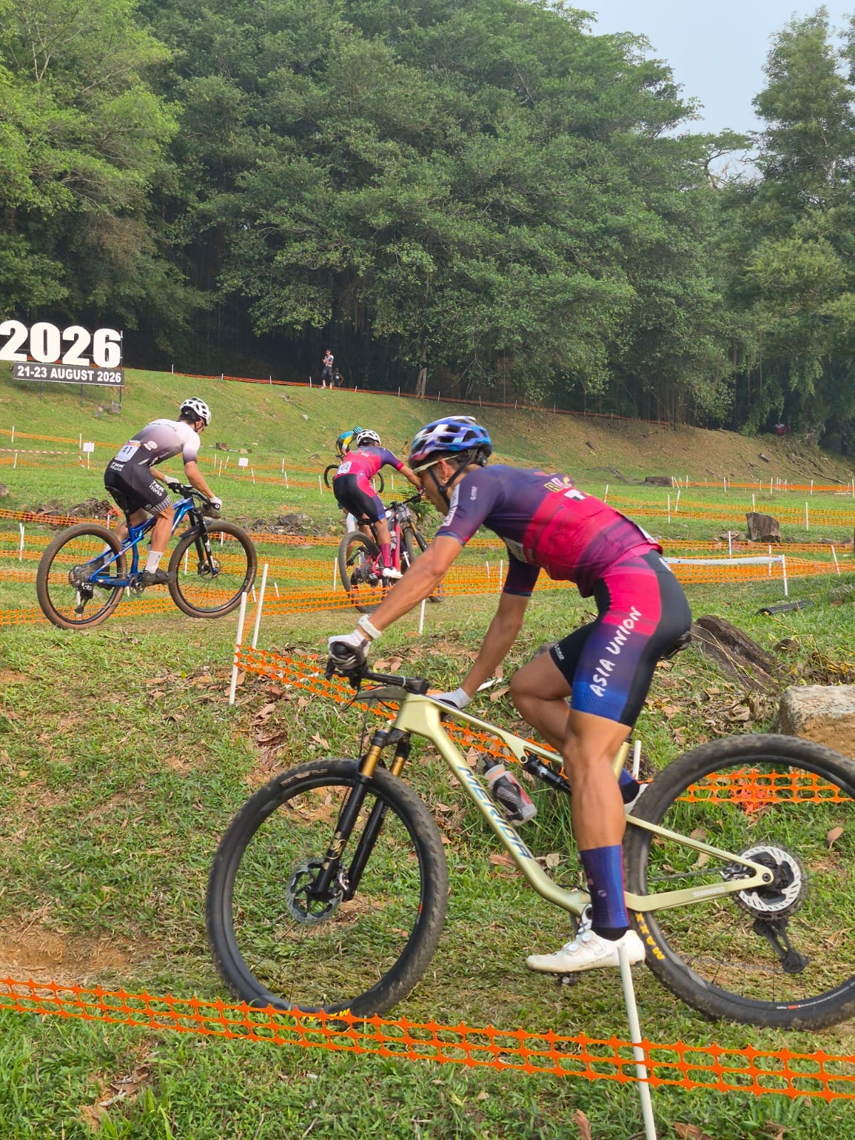 Mountain bike racer on a track beside orange safety fencing.